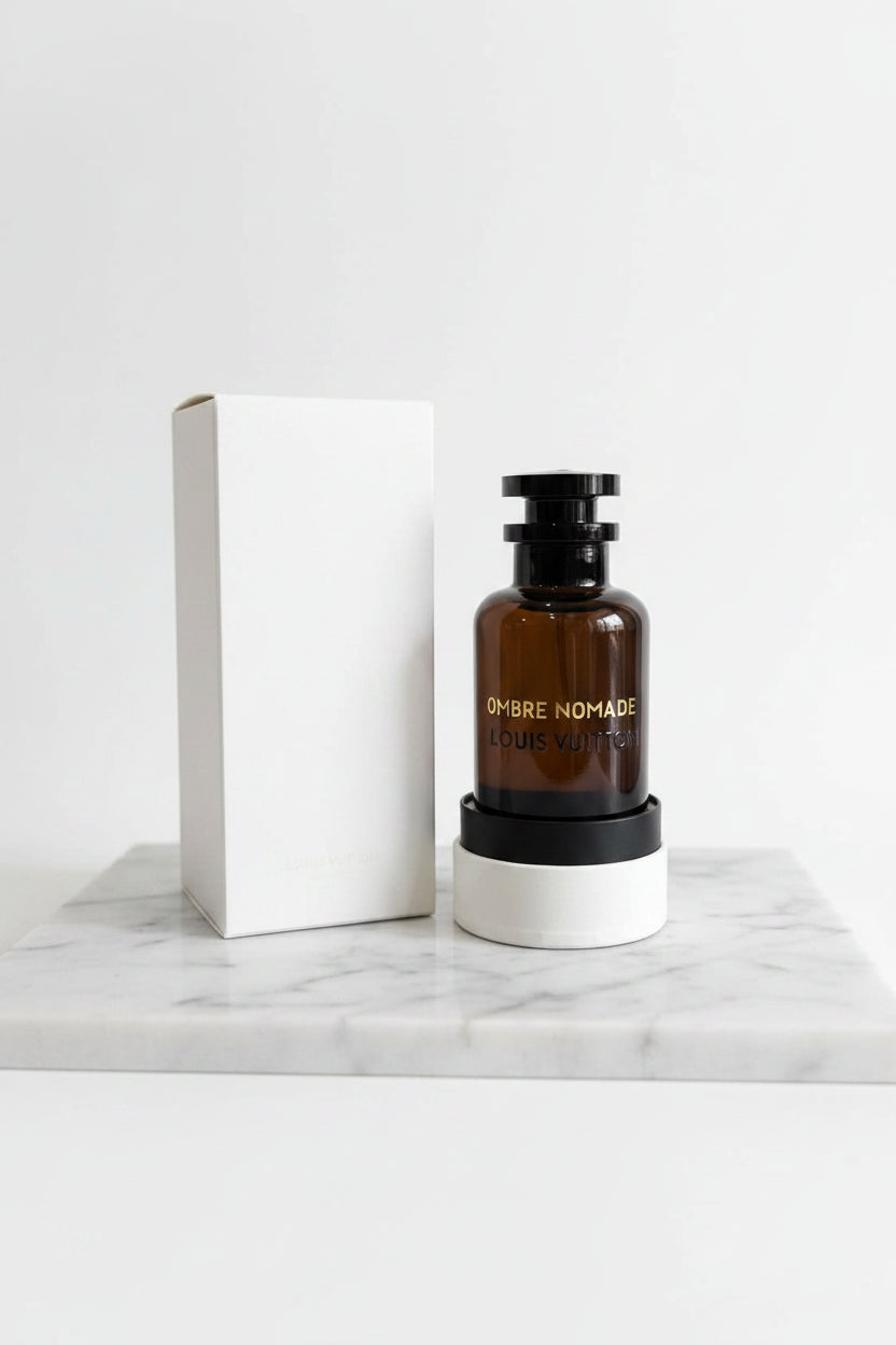 Black perfume bottle labeled 'Ombre Nomade' with a white box and white container in the background.